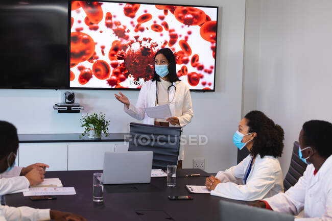 Doctora con mascarilla para la cara presentando al equipo de doctores en la sala de reuniones. salud e investigación médica durante la pandemia de covid 19 - foto de stock