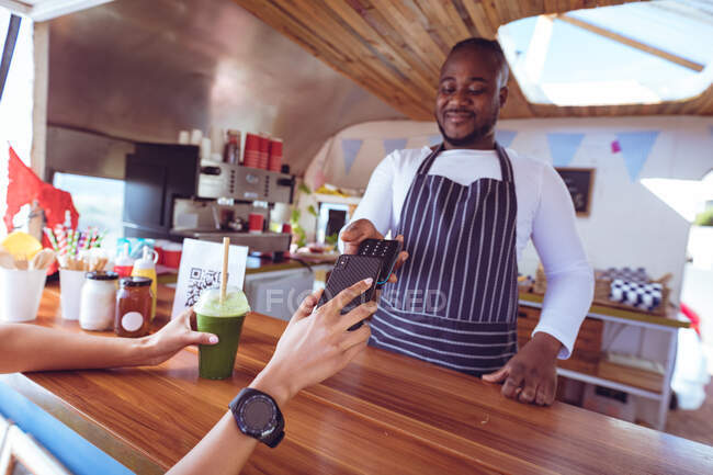 African american man in food truck taking smartphone payment holding terminal. independent business and street food service concept. — Stock Photo