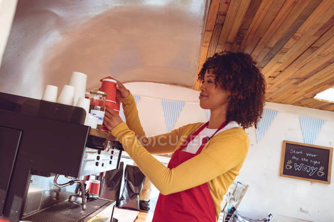Mixed race woman preparing coffee by coffee machine in food truck. independent business and street food service concept. — Stock Photo
