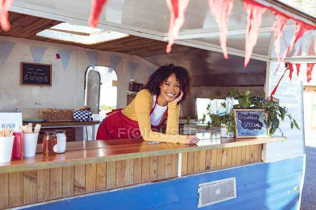 Portrait d'une femme souriante de race mixte penchée sur le comptoir dans un camion de nourriture. entreprise indépendante et concept de service de restauration de rue. — Photo de stock