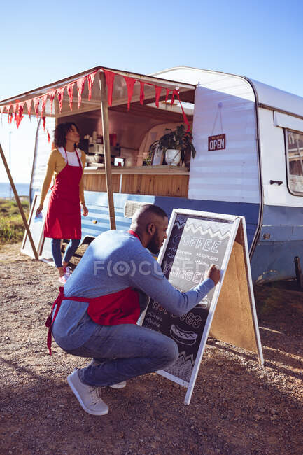 Diverse Paare öffnen und bereiten Food Truck am Meer an einem sonnigen Tag, Mann schreibt auf Speisekarte. Unabhängiges Geschäfts- und Streetfood-Konzept. — Stockfoto