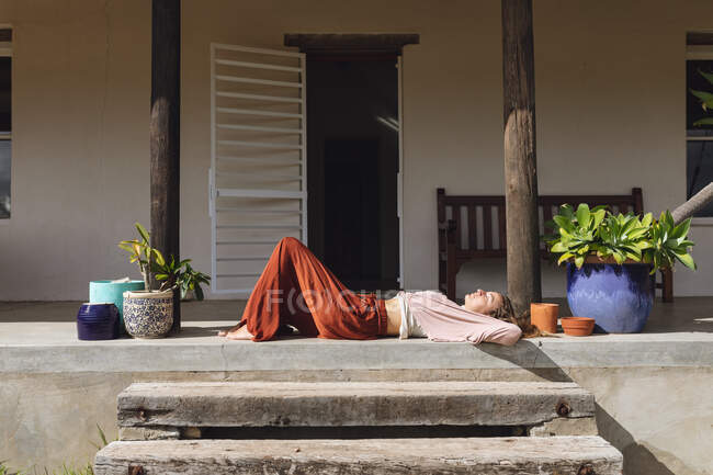 Mulher caucasiana feliz relaxante deitado no terraço ensolarado casa de campo. vida saudável, perto da natureza em fora da grade casa rural. — Fotografia de Stock