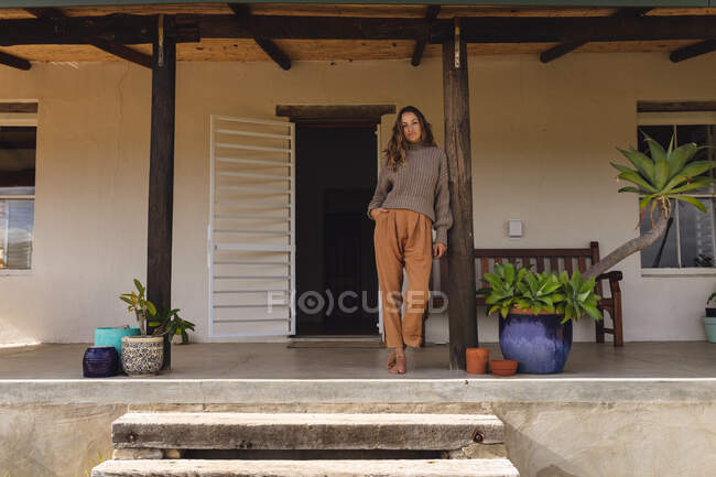 Mulher caucasiana relaxada em pé no terraço da casa de campo, apoiada em pilar de madeira. vida saudável, perto da natureza em fora da grade casa rural. — Fotografia de Stock