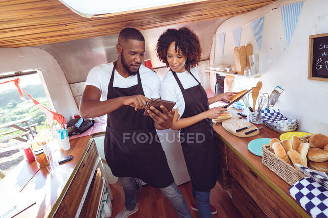 Diversa pareja detrás del mostrador utilizando la tableta en camión de alimentos. concepto de empresa independiente y servicio de comida callejera. - foto de stock