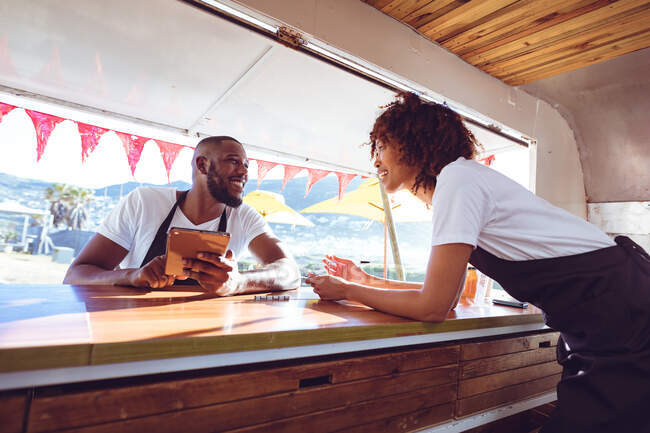 Sorridente coppia diversificata appoggiata sul bancone utilizzando tablet in camion cibo. concetto indipendente di business e street food. — Foto stock