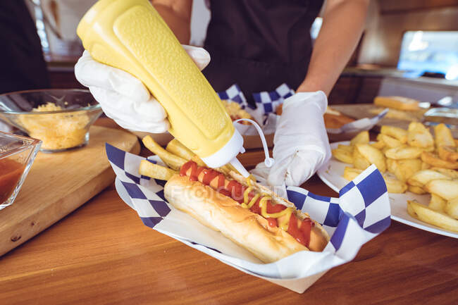 Mitte Frau gießt Senf auf Hot Dog hinter Theke in Food Truck. Unabhängiges Geschäfts- und Streetfood-Konzept. — Stockfoto