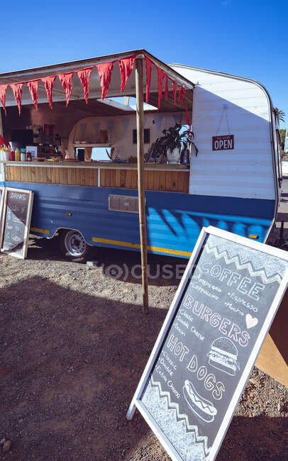 General view of food truck with red bunting and menu board against blue sky. independent business and street food service concept. — Stock Photo