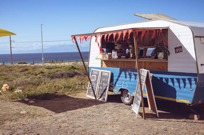 Vista general del camión de comida con bollería roja junto al mar en un día soleado. concepto de empresa independiente y servicio de comida callejera. - foto de stock