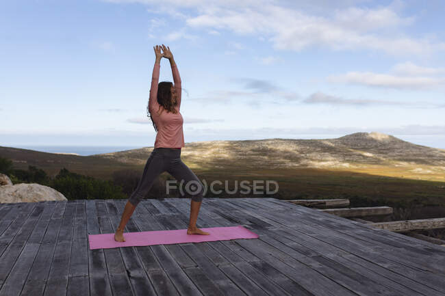 Щаслива біла жінка практикує йогу, стоячи на палубі, що тягнеться в сільській місцевості. здорове життя, поза мережею і близькість до природи . — стокове фото