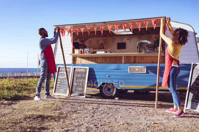 Coppia diversificata apertura e preparazione camion cibo al mare nella giornata di sole. concetto indipendente di business e street food. — Foto stock