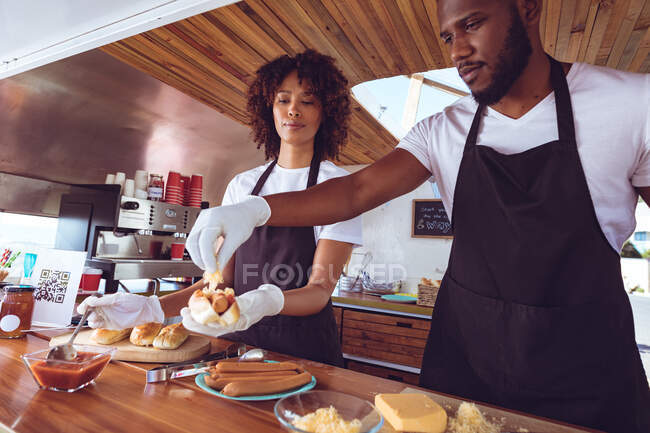 Diverse Paare bereiten hinter der Theke im Food-Truck Hot Dogs zu. Unabhängiges Geschäfts- und Streetfood-Konzept. — Stockfoto