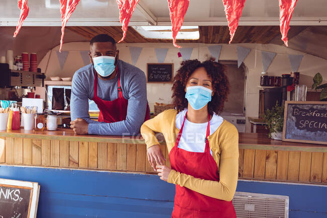 Portrait of diverse couple wearing face masks in food truck. independent business and street food service during covid 19 pandemic concept. — Stock Photo