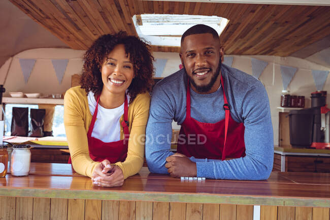 Portrait of smiling diverse couple behind counter in food truck. independent business and street food service concept. — Stock Photo