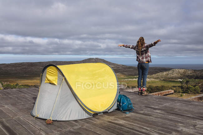Visão traseira da mulher caucasiana acampar, de pé fora da tenda no convés da montanha, braços estendidos. vida saudável, fora da grade e perto da natureza. — Fotografia de Stock