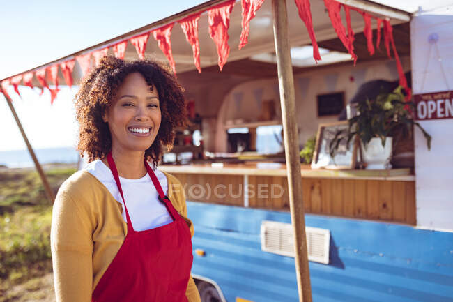 Retrato de mulher de raça mista sorridente em pé junto caminhão de comida no dia ensolarado. conceito independente de serviço de negócios e comida de rua. — Fotografia de Stock