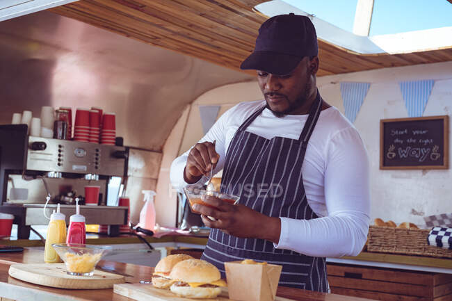 African american man in food truck preparing order with hamburgers on worktop. independent business and street food service concept. — Stock Photo