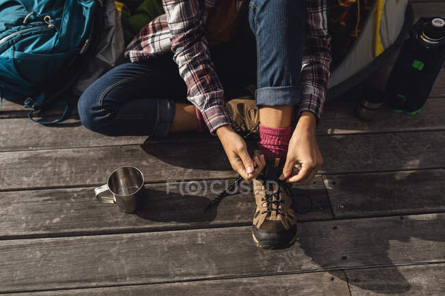 Baixa seção de mulher acampar, sentado fora da tenda no convés colocando botas. vida saudável, fora da grade e perto da natureza. — Fotografia de Stock