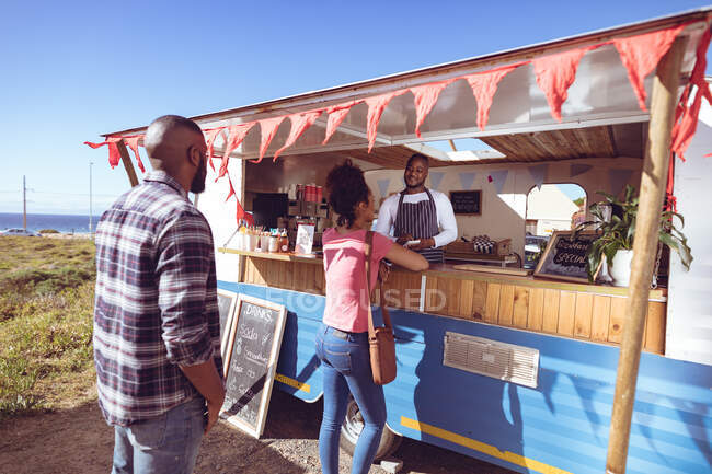 Smiling african american man in food truck taking order from female customer. independent business and street food service concept. — Stock Photo