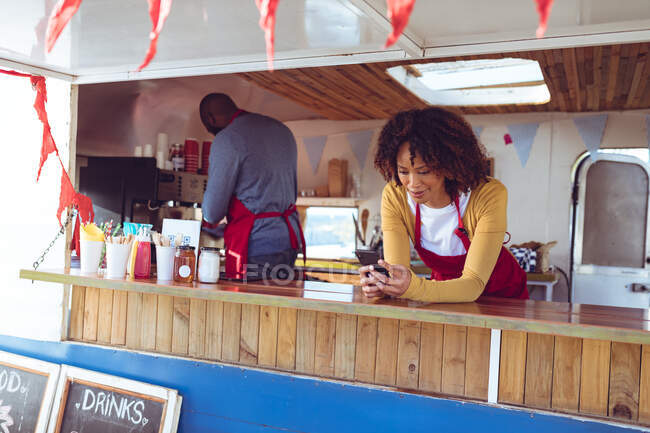 Donna razza mista utilizzando smartphone appoggiato sul bancone nel camion cibo. concetto indipendente di business e street food. — Foto stock