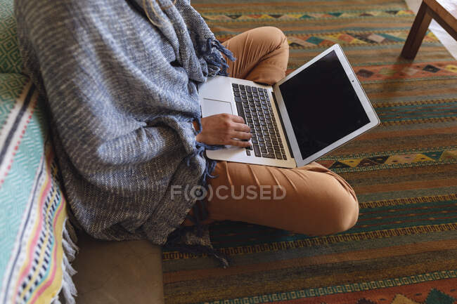 Low section of woman with blanket sitting on floor using laptop in cottage living room. simple living in an off the grid rural home. — Stock Photo