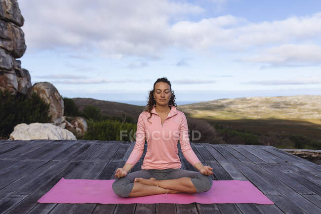 Glückliche kaukasische Frau praktiziert Yoga sitzend in Meditation in ländlicher Berglandschaft. gesundes Leben, netzfrei und naturnah. — Stockfoto