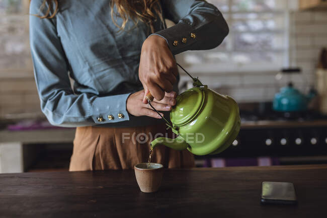 Midsection de la femme debout dans la cuisine du chalet versant le thé de la théière. vivre simplement dans une maison rurale hors réseau. — Photo de stock