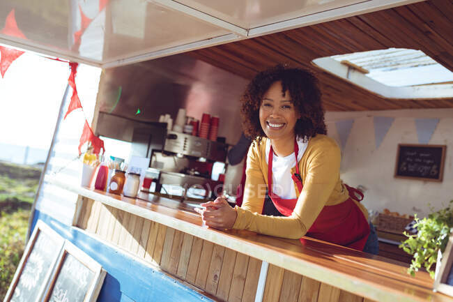 Портрет улыбающейся женщины смешанной расы, опирающейся на прилавок в фургоне с едой. независимая концепция обслуживания бизнеса и уличной еды. — стоковое фото