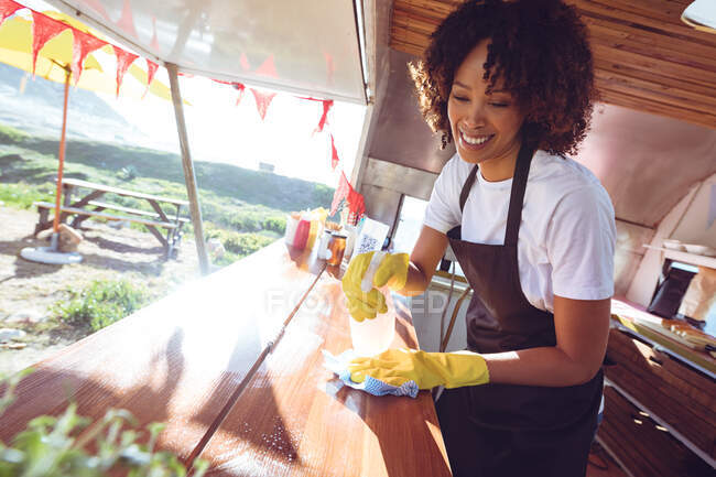 Smiling mixed race woman cleaning counter in food truck. independent business and street food service concept. — Stock Photo