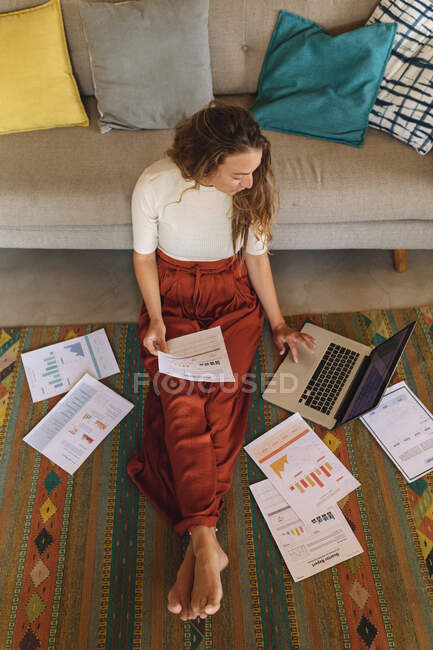 Caucasian woman working at home sitting on floor with paperwork using laptop. working at home in isolation during quarantine lockdown. — Stock Photo