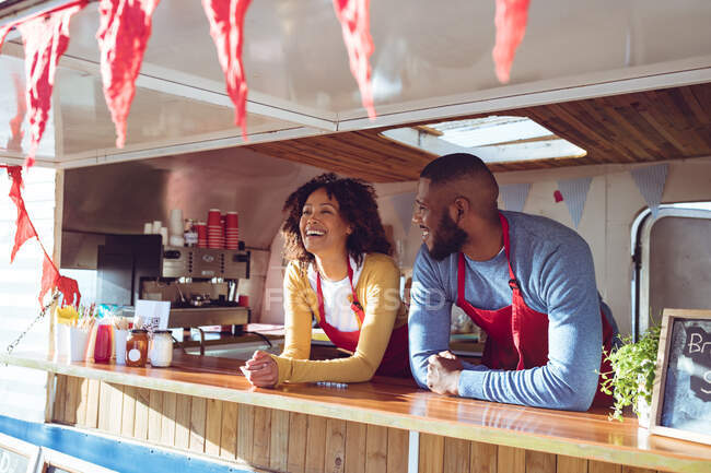Smiling diverse couple behind counter in food truck on sunny day. independent business and street food service concept. — Stock Photo