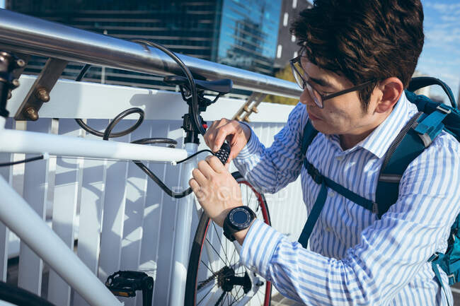 Uomo d'affari asiatico che blocca la bicicletta alle ringhiere in strada con edifici moderni sullo sfondo. uomo d'affari in giro per la città concetto. — Foto stock