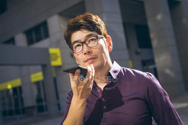 Asiatischer Geschäftsmann, der auf einer Straße in der Stadt mit dem Smartphone spricht. Digitaler Nomade im Stadtkonzept unterwegs. — Stockfoto