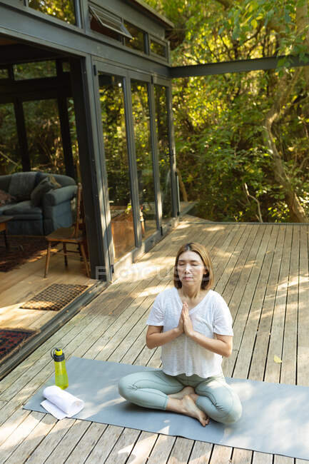 Азиатка практикует йогу с закрытыми глазами на террасе в саду. в доме в изоляции во время карантинной изоляции. — стоковое фото