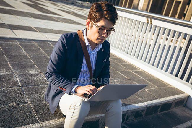 Hombre de negocios asiático usando portátil sentado en los escalones de la calle de la ciudad. nómada digital en concepto de ciudad. - foto de stock