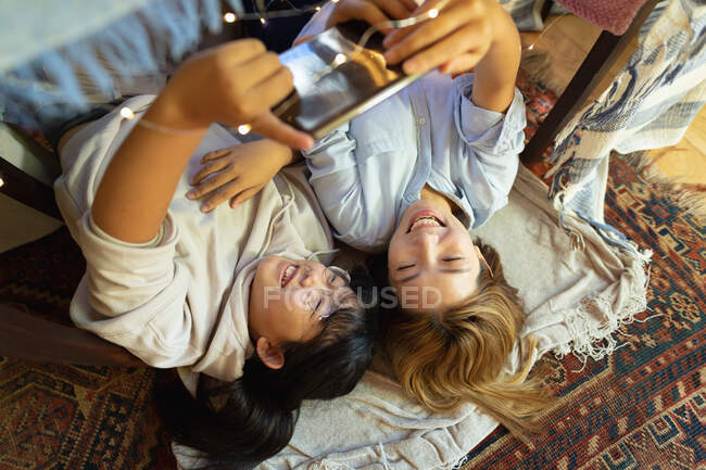 Посміхаючись, азіатська жінка з донькою використовувала таблетку, яка лежала під ковдральним наметом. вдома в ізоляції під час карантину.. — стокове фото