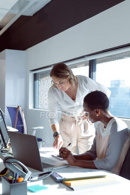 Dos diversas empresarias sonrientes trabajando juntas, usando laptop, hablando. negocio creativo independiente en una oficina moderna. - foto de stock