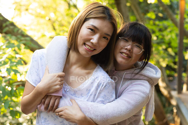 Retrato de mujer asiática sonriente con su hija abrazándose en el jardín. en casa en aislamiento durante el bloqueo de cuarentena. - foto de stock