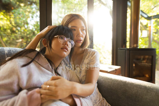 Retrato de mujer asiática triste con su hija abrazándose sentada en el sofá. en casa en aislamiento durante el bloqueo de cuarentena. - foto de stock