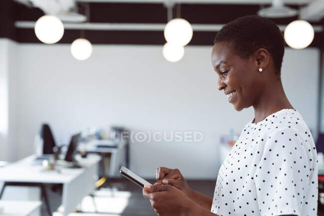 Empresária afro-americana sorrindo usando tablet no trabalho. negócio criativo independente em um escritório moderno. — Fotografia de Stock