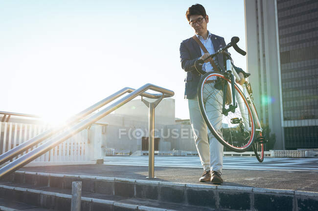 Midsection de hombre de negocios asiático llevando su bicicleta en la calle de la ciudad. hombre de negocios fuera y alrededor en concepto de ciudad. - foto de stock