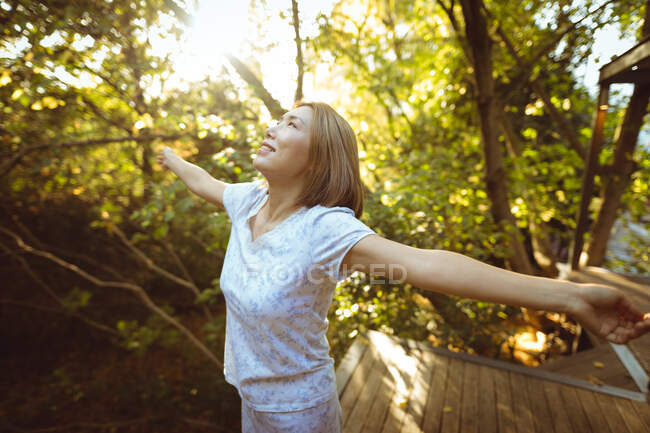 Smiling asian woman in pyjamas with her arms outstretched in garden. at home in isolation during quarantine lockdown. — Stock Photo