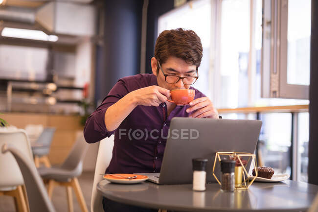 Asian businessman using laptop drinking coffee in cafe. business travel, digital nomad on the go out and about in city concept. — Stock Photo