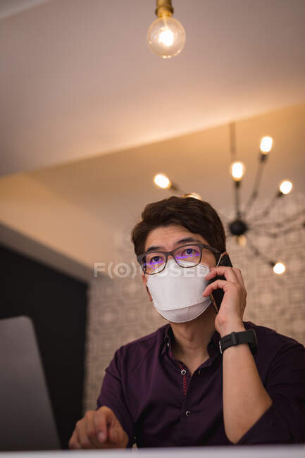 Asian businessman wearing face mask using smartphone in hotel lobby. digital nomad out and about in city during covid 19 pandemic concept. — Stock Photo