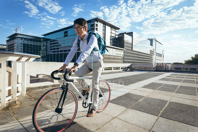Asiatischer Geschäftsmann mit Fahrrad in der Stadtstraße mit modernen Gebäuden im Hintergrund. Geschäftsmann im Stadtkonzept unterwegs. — Stockfoto