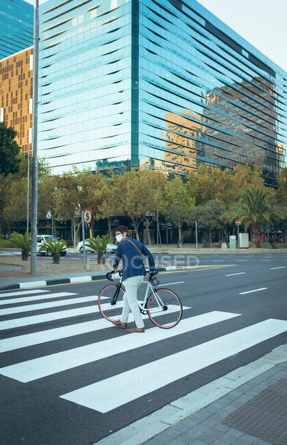 Asian businessman wearing face mask crossing city street with modern buildings in background. businessman out and about in city during covid 19 pandemic concept. — Stock Photo