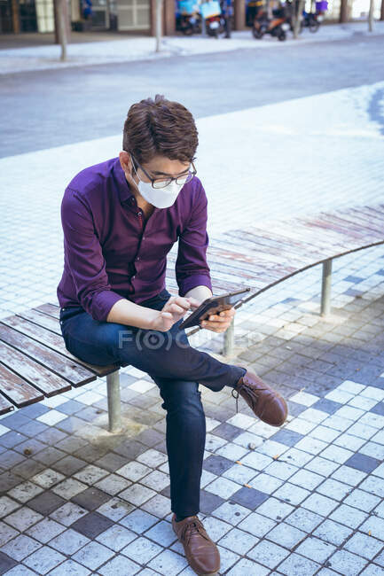 Asian businessman wearing face mask using tablet in city street. digital nomad out and about in city during covid 19 pandemic concept. — Stock Photo