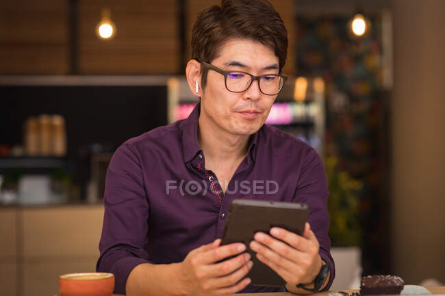 Asiatischer Geschäftsmann mit Tablet und drahtlosen Kopfhörern im Café. Geschäftsreisen, digitaler Nomade unterwegs im Stadtkonzept. — Stockfoto