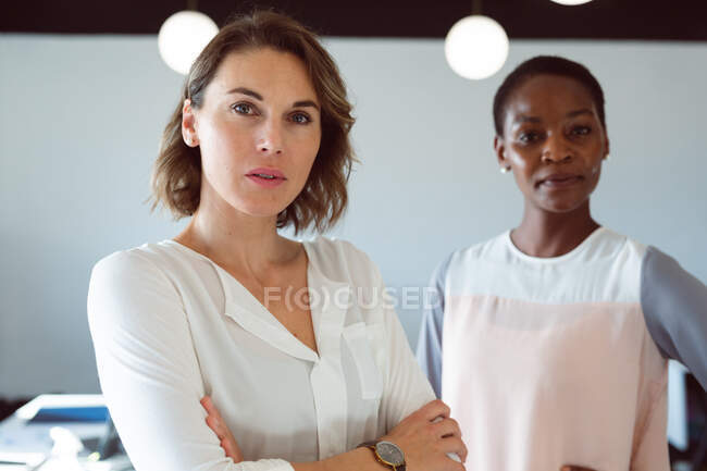 Две разноплановые деловые женщины, стоящие со скрещенными руками на работе. креативный бизнес в современном офисе. — стоковое фото