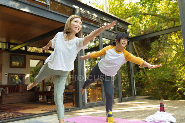 Lächelnde Asiatin und ihre Tochter praktizieren Yoga auf der Terrasse im Garten. Zuhause in Isolation während der Quarantäne. — Stockfoto