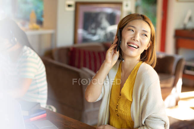 Sorridente donna asiatica che parla su smartphone, lavora da casa. a casa isolata durante l'isolamento in quarantena. — Foto stock